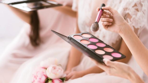 Eine Frau hält eine Palette mit Rouge und einen Pinsel in der Hand.