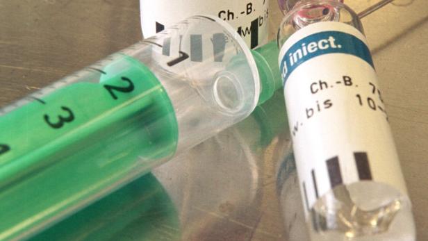 Eine Spritze und eine Ampulle mit Medikamenten liegen auf einer Oberfläche.