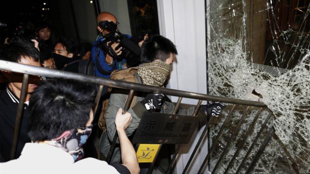 Eine Menschenmenge steht vor einem Gebäude mit eingeschlagener Scheibe.