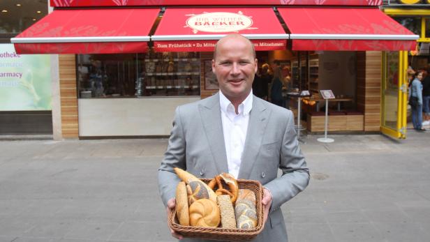 Ein Mann im Anzug präsentiert einen Korb mit Backwaren vor der Bäckerei „Ihr Witte Bäcker“.