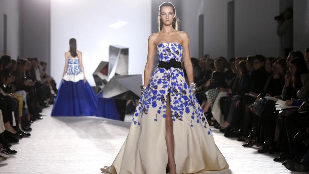 Eine Frau in einem trägerlosen, bodenlangen Kleid mit blauem Blumenmuster auf einem Laufsteg.