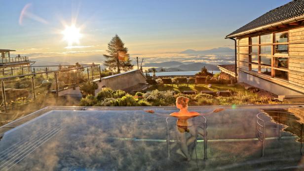 Eine Frau entspannt in einem Pool mit Blick auf eine Berglandschaft bei Sonnenaufgang.