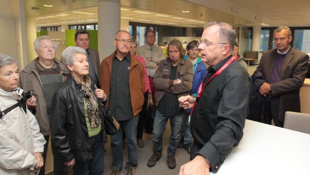 Eine Gruppe von Menschen steht in einem hellen Raum und hört aufmerksam zu.