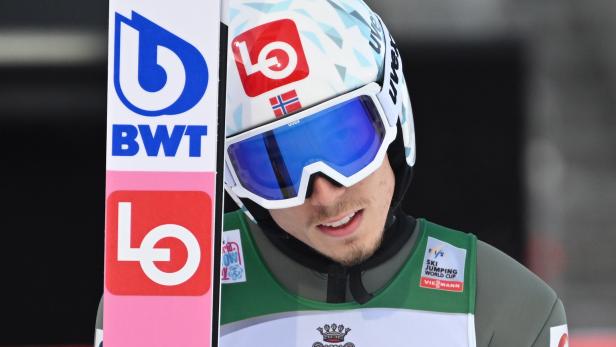 Ein Skispringer mit Helm und Skibrille hält einen Ski mit Sponsorenlogos.