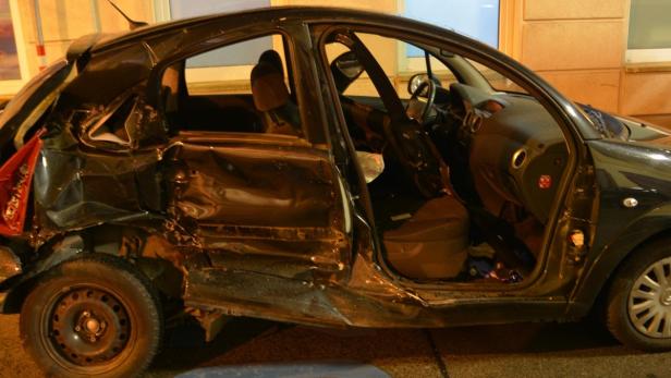 Ein schwarzes Auto mit schweren Schäden an der Seite und am Heck.