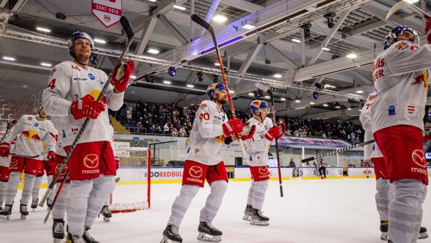 Eishockeyspieler der Red Bulls stehen auf dem Eis und halten ihre Schläger hoch.