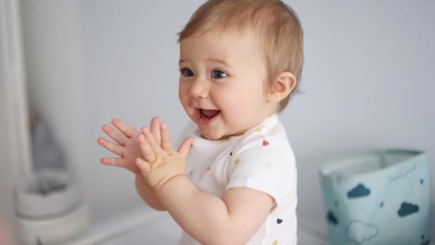 Ein lachendes Baby klatscht in die Hände.