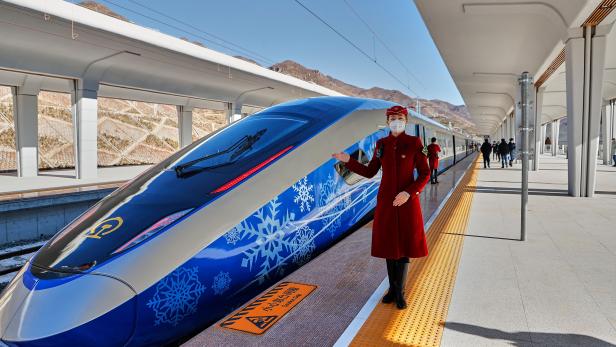 Eine Zugbegleiterin steht vor einem blau-weißem Hochgeschwindigkeitszug auf einem Bahnsteig.