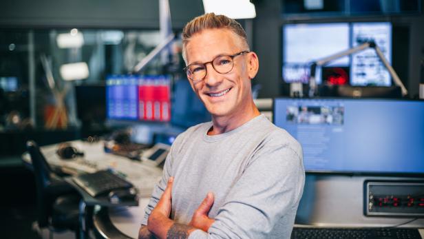 Ein Mann mit Brille lächelt in einem Radiostudio in die Kamera.