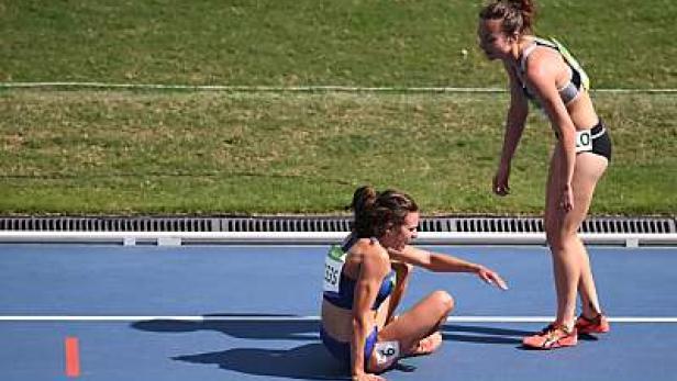 Eine Athletin sitzt erschöpft auf der blauen Laufbahn, während eine andere ihr hilft.