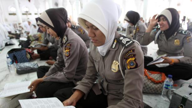 Mehrere Polizistinnen mit Hijab sitzen auf dem Boden und lesen in Büchern.