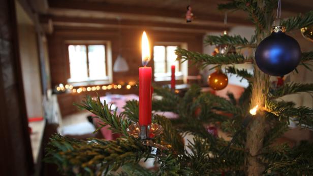 Eine brennende rote Kerze auf einem Weihnachtsbaum mit blauer Kugel.
