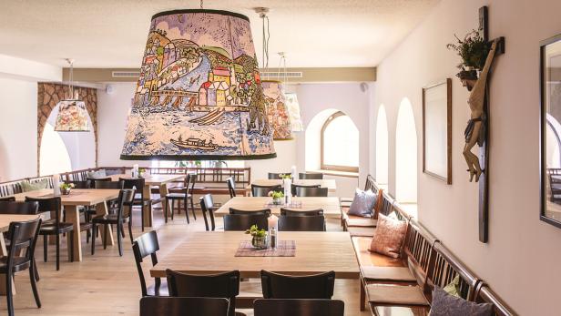 Ein Speisesaal mit Holztischen, Stühlen und Lampen mit Flusslandschaftsmotiven.