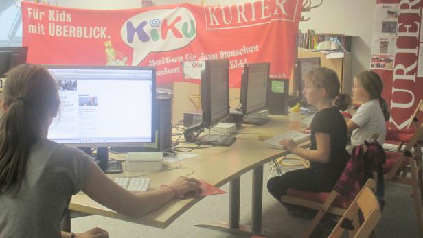Drei Mädchen arbeiten an Computern vor einem Banner des „Kiku Kurier“.