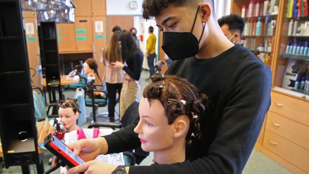 Handy statt Schulbuch: Muhammet Cetin muss die abgebildete Frisur nachmachen – das trainiert die Feinmotorik