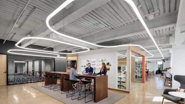 Drei Personen sitzen an einem Stehtisch in einem modernen Büro.