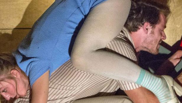 Eine Frau liegt auf einem Mann in einem engen Raum.