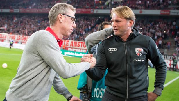 Zwei Männer schütteln sich auf einem Fußballfeld die Hände.