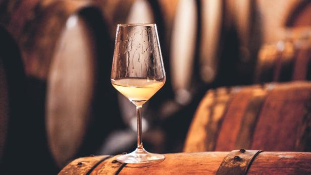 Ein Glas Weißwein steht auf einem Holzfass.