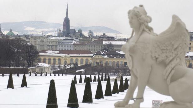 Blick über einen verschneiten Park auf Wien mit einer Sphinx-Statue im Vordergrund.
