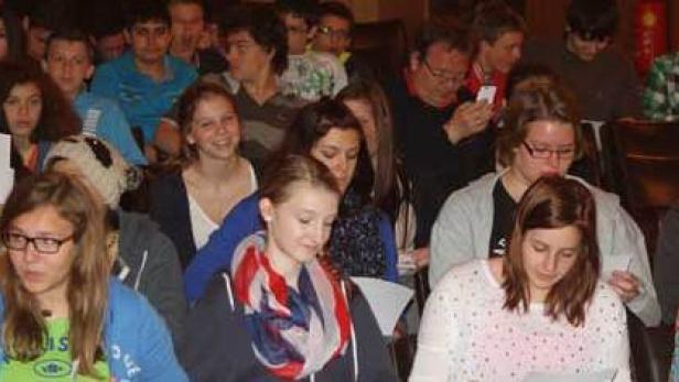 Eine Gruppe von Jugendlichen sitzt in einem Raum und schaut in eine Richtung.