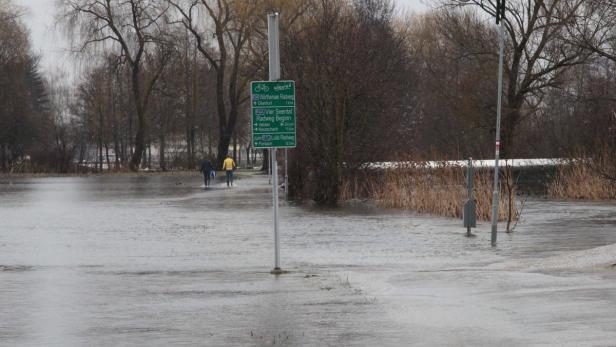 Überschwemmung auf einem Radweg; zwei Personen waten durch das Wasser.