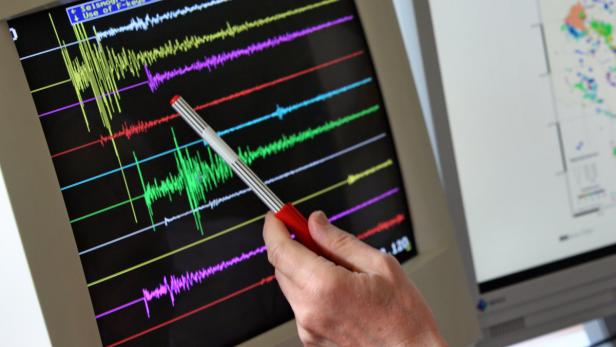 Eine Hand zeigt mit einem Stift auf einen Bildschirm mit Seismographenlinien.