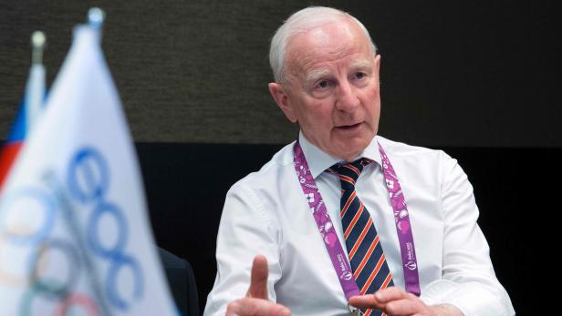 Ein Mann mit Krawatte und Lanyard spricht vor einer Flagge.