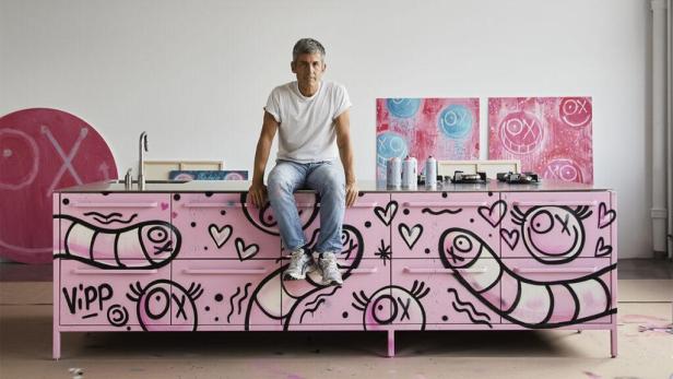 André Saraiva sitzt auf einer rosa Kücheninsel, die mit Graffiti verziert ist.