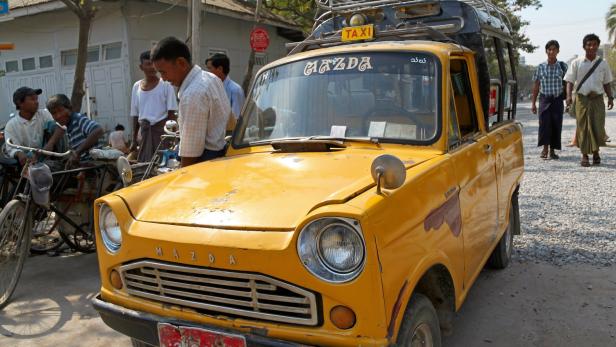 Ein gelbes Mazda-Taxi steht auf einer Straße in Myanmar.