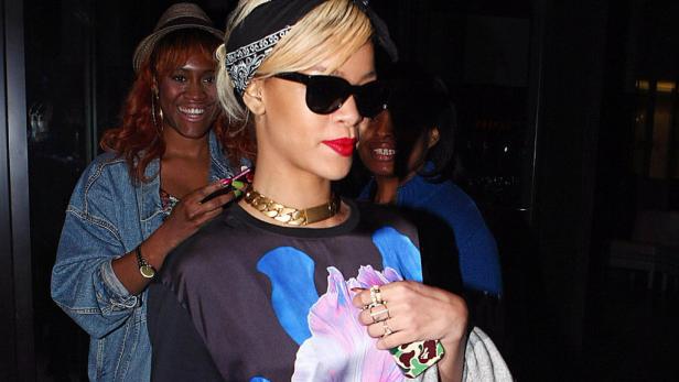 Rihanna mit Sonnenbrille und Kopftuch, umgeben von zwei Frauen.