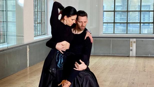 Ein Tanzpaar in schwarzer Kleidung tanzt in einem hellen Raum.