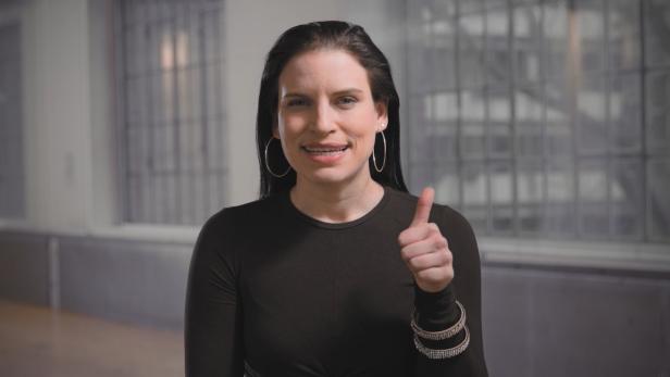 Eine Frau mit Zahnspange lächelt und zeigt den Daumen nach oben.