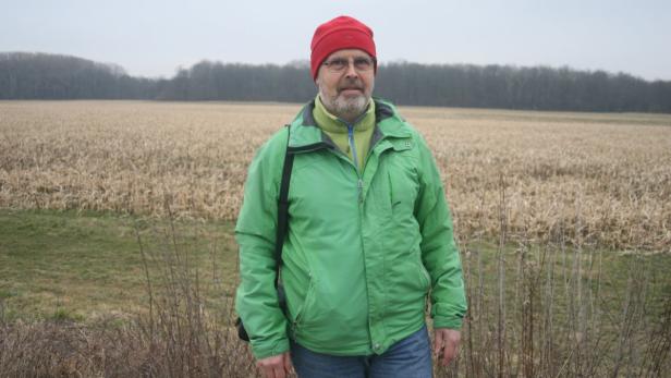 Ein Mann mit roter Mütze und grüner Jacke steht vor einem Feld.