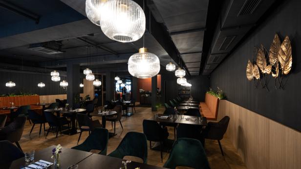 Innenansicht eines eleganten Restaurants mit dunklen Tischen und Stühlen unter dekorativen Lampen.