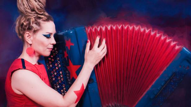 Eine Frau mit Dreadlocks spielt auf einem rot-blauen Akkordeon mit Sternen.