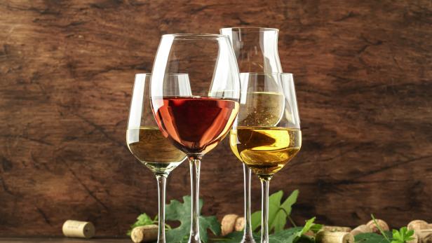 Mehrere Gläser mit Weißwein und Roséwein stehen auf einem Holztisch.