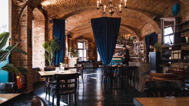 Innenansicht eines Restaurants mit Ziegelgewölbe und blauen Vorhängen.