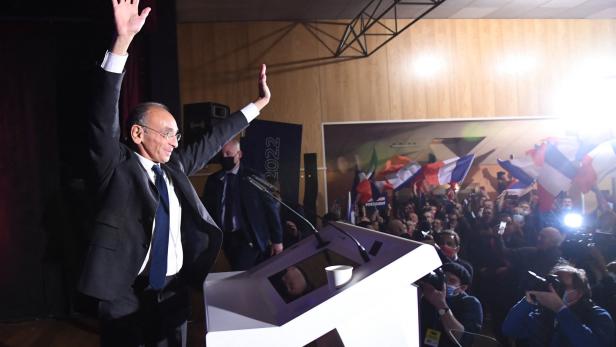 Éric Zemmour steht auf einer Bühne und winkt seinen Anhängern zu.