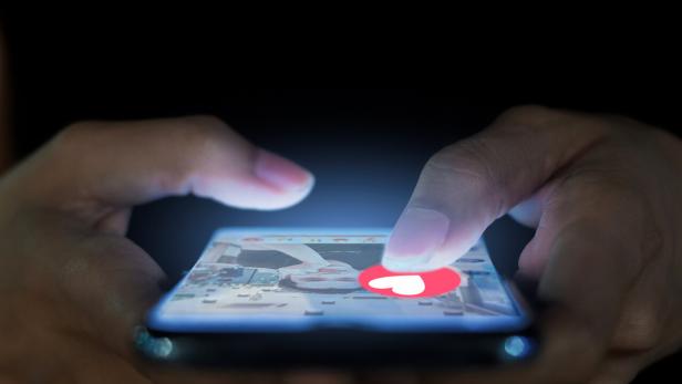Eine Person tippt auf ein Smartphone mit einem roten Herz-Symbol auf dem Bildschirm.