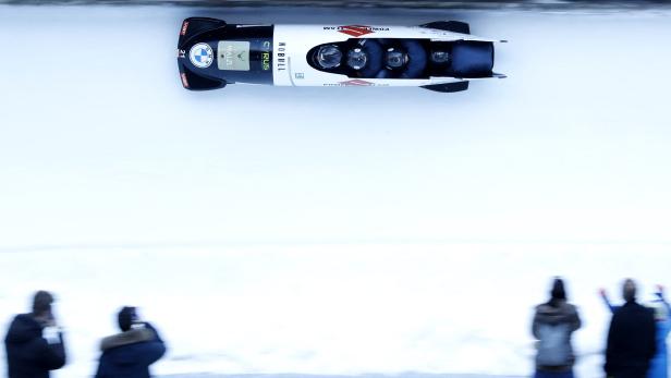 Ein Viererbob rast auf einer Eisbahn, beobachtet von Zuschauern.