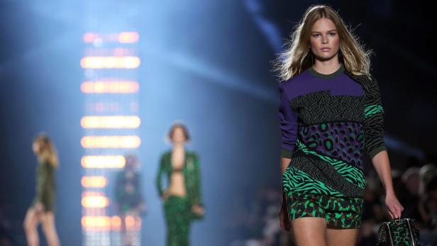 Eine blonde Frau auf dem Laufsteg präsentiert ein farbenfrohes Outfit mit Tiermustern.