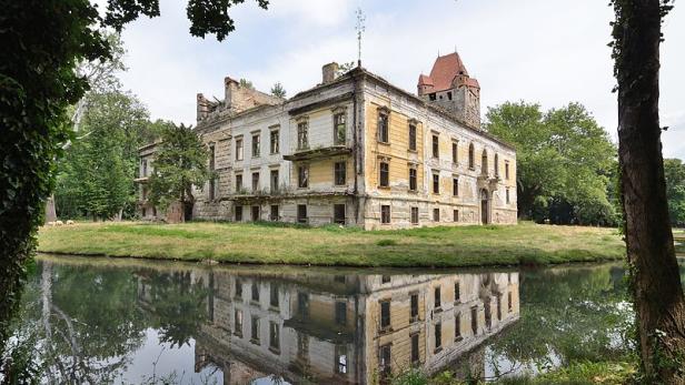Ein verfallenes Schloss mit einem roten Turm spiegelt sich im Wasser.