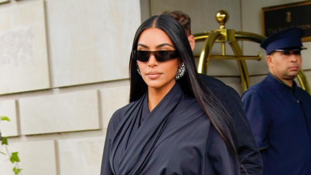 Kim Kardashian verlässt ein Gebäude in einem schwarzen Outfit und Sonnenbrille.