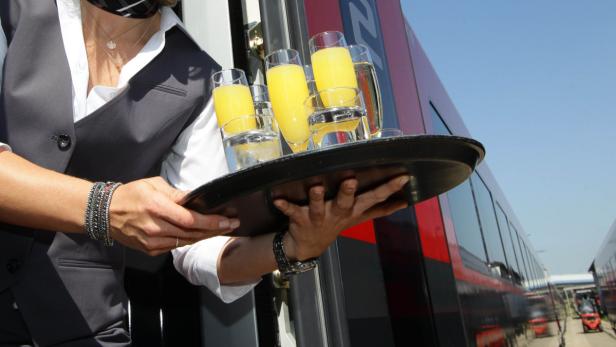 Eine Person im Service hält ein Tablett mit Getränken vor einem Zug bereit.