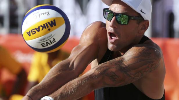 Ein Beachvolleyballspieler mit Tätowierungen baggert einen Ball.