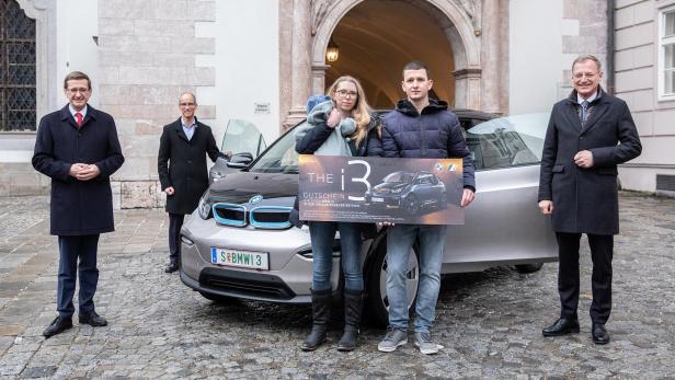 Ein Paar hält einen Gutschein für einen BMW i3 vor einem grauen BMW i3.