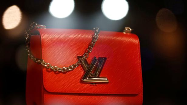 Eine rote Louis Vuitton Handtasche mit silberner Kette und Logo vor dunklem Hintergrund.