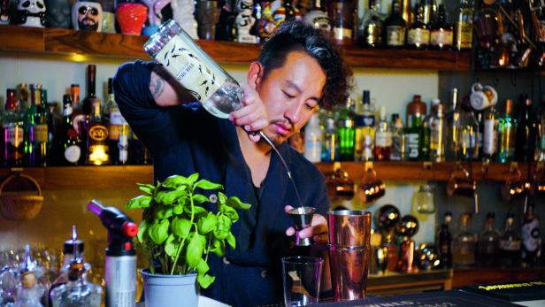 Ein Barkeeper gießt eine Flüssigkeit in einen Messbecher vor einer Bar.