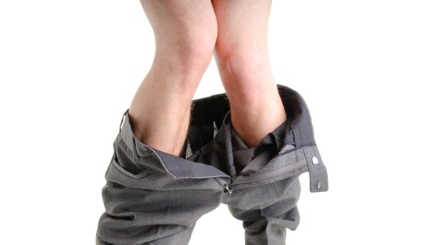 Eine Person mit heruntergelassener Hose steht vor einem weißen Hintergrund.